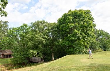 golfer teeing off with log cabins in background