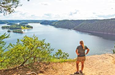 woman in shorts and t-shirt looking over Dale Hollow Lake from Eagle Point overlook. Blue sky and islands in the distance.